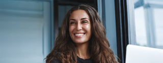 Smiling woman with long hair sitting by window – Sagrada BioSkincare Press Page Hero