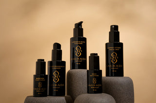 Signature collection of Sagrada bioskincare products in black bottles with gold branding, elegantly displayed on stone pedestals against a soft beige background