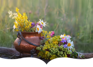 A copper pot filled with freshly picked wildflowers, including daisies and yellow blooms, set against a lush green meadow background.