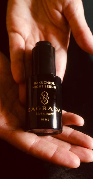 Hands cradling a black bottle of Sagrada Bakuchiol Night Serum, featuring gold branding, set against a dark background.