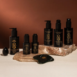 Full Sagrada BioSkincare collection displayed on natural stone, featuring cleansers, serums, mist, lube, gua sha, and yoni egg for holistic self-care