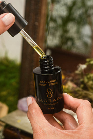 Applying Sagrada Bakuchiol Night Serum with a dropper in a botanical setting, highlighting a clean nighttime skincare ritual