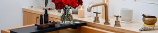 Sagrada BioSkincare Bakuchiol Night Serum and Copper Vetiver Facial Mist displayed on a wooden tray by a bath with flowing water and fresh red roses.