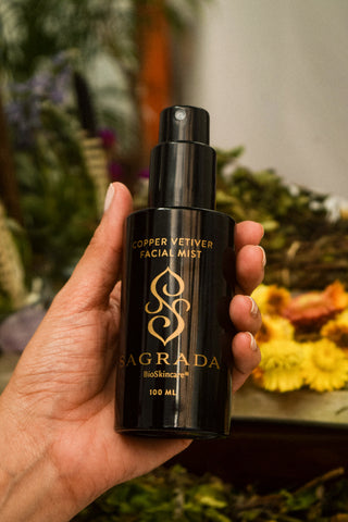 Hand holding Sagrada Copper Vetiver Facial Mist surrounded by natural flowers and plants, reflecting clean, plant-based skincare rituals