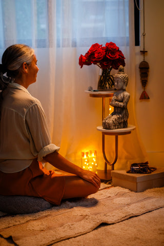 Woman seated in meditation by a sacred altar with roses and soft lighting, reflecting a sensual and intentional self-care ritual with Sagrada Lube for Her