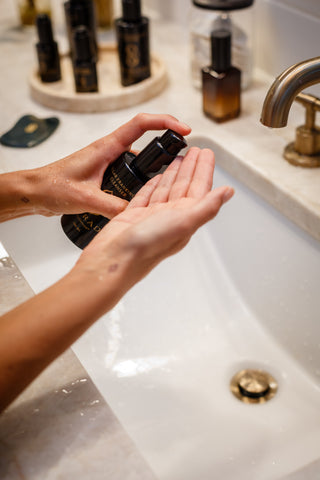 Hands dispensing Sagrada Micellar Frankincense Cleanser at the bathroom sink, highlighting a gentle and intentional cleansing ritual