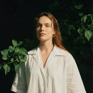 Woman standing in natural sunlight surrounded by green leaves, representing Sagrada’s clean botanical skincare philosophy