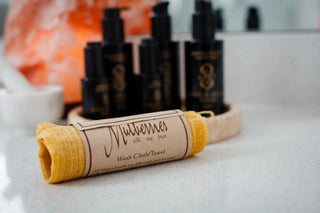 Mulberries silk tea fruit washcloth towel rolled on a bathroom counter, with Sagrada BioSkincare products arranged in the background near a salt lamp.