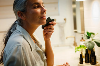 Woman using a gua sha stone for facial massage during her skincare ritual, with Sagrada BioSkincare products visible in the background.